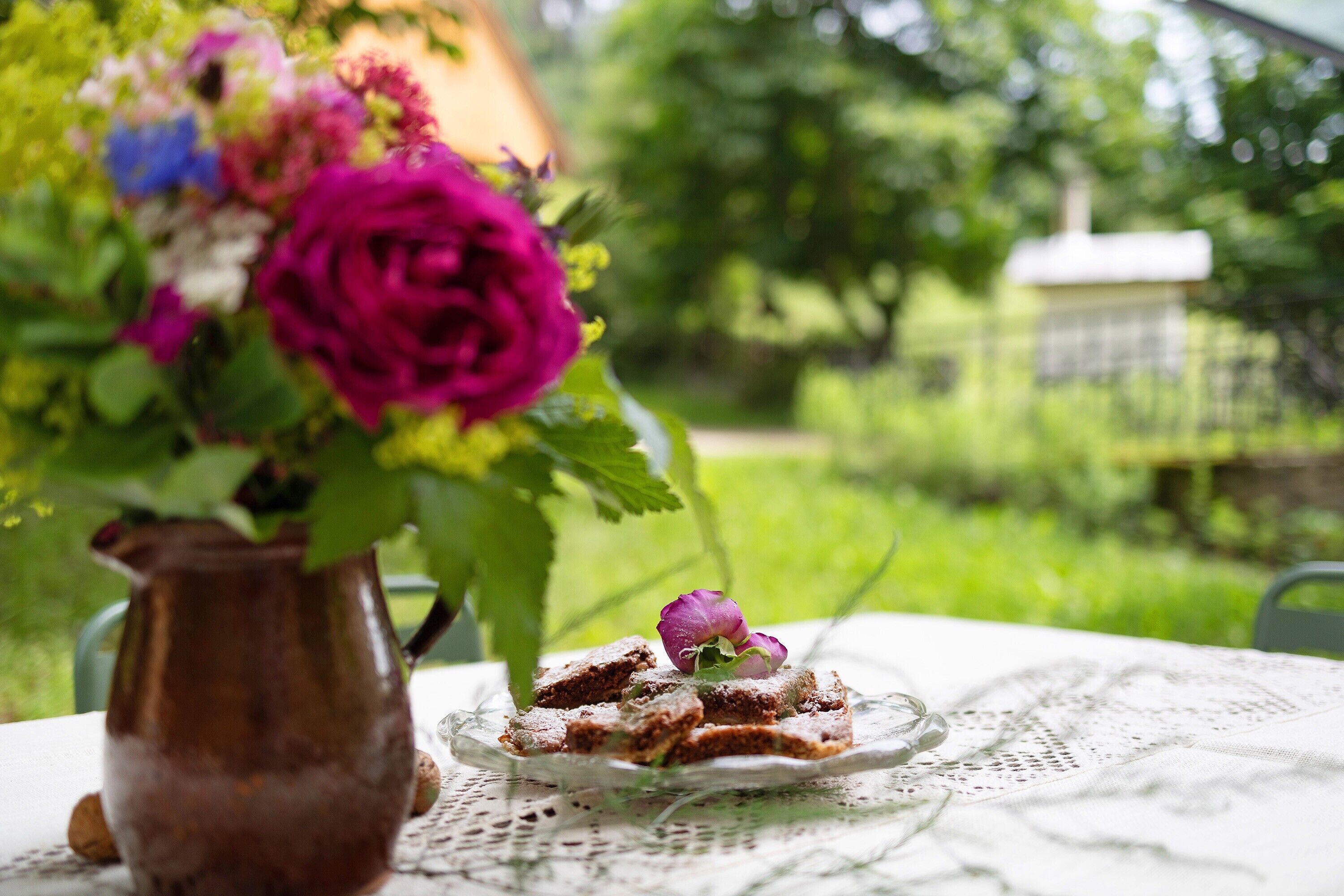 A table with a lace tablecloth, a pitcher, and a plate with food and a flower.
