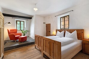 Ein Schlafzimmer mit einem hölzernen Bett, einem roten Sessel, einem kleinen Tisch und einem Fenster.