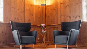 Deux fauteuils gris, une petite table ronde ornée d’un vase de fleurs et un lampadaire dans une pièce aux murs lambrissés.