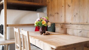 Une table en bois avec un vase de fleurs, une chaise et, au fond, un lit superposé.