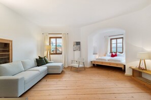 A room with a sofa, a chair, a bed, a wooden floor, and a window with a view.