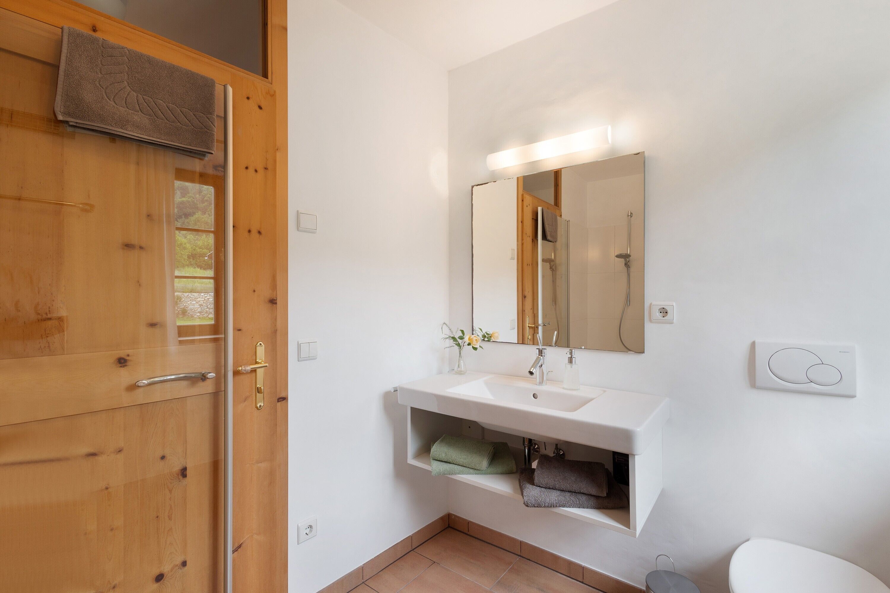 Un baño con puerta de madera, lavamanos blanco, espejo y retrete.