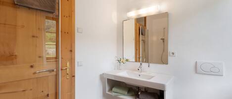 Un baño con puerta de madera, lavamanos blanco, espejo y retrete.