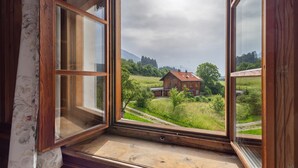 A wooden window frame with a view of a rural landscape, including a house and greenery.