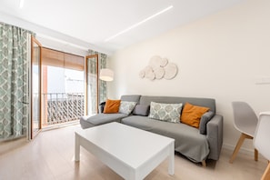 A living room with a grey sofa, white coffee table, and a balcony with patterned curtains.