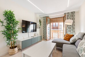 A modern living room with a flat-screen TV, a large potted plant, a grey sofa, and a white coffee table. - Apartment "Andalucía Centro" with Balcony & Wi-Fi (Antequera)