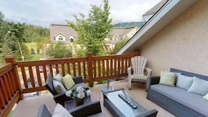A balcony with a wooden railing, a sofa, a chair, and a small table with a remote control. - Large 2 bedroom at Riverside / Great Location (Fernie)