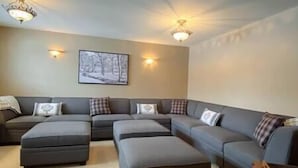 A living room with a sectional sofa, ottomans, and wall-mounted lighting. - Large 2 bedroom at Riverside / Great Location (Fernie)