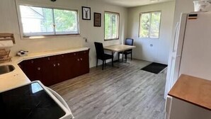 A kitchen with a dining table and chairs, a refrigerator, and a window with a view of trees. - Puma's executive cat house! (Fernie)