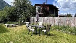 A patio with a table and chairs, a wooden fence, and a building in the background. - Puma's executive cat house! (Fernie)