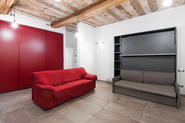 A room with a red sofa, a grey bench, a wooden ceiling, and white walls.
