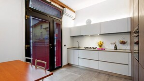 A compact kitchen with a dining table, built-in cabinets, and a window with blinds. - Apartment 'La Sartoria' with Dedicated Parking and Air Conditioning (Porlezza)