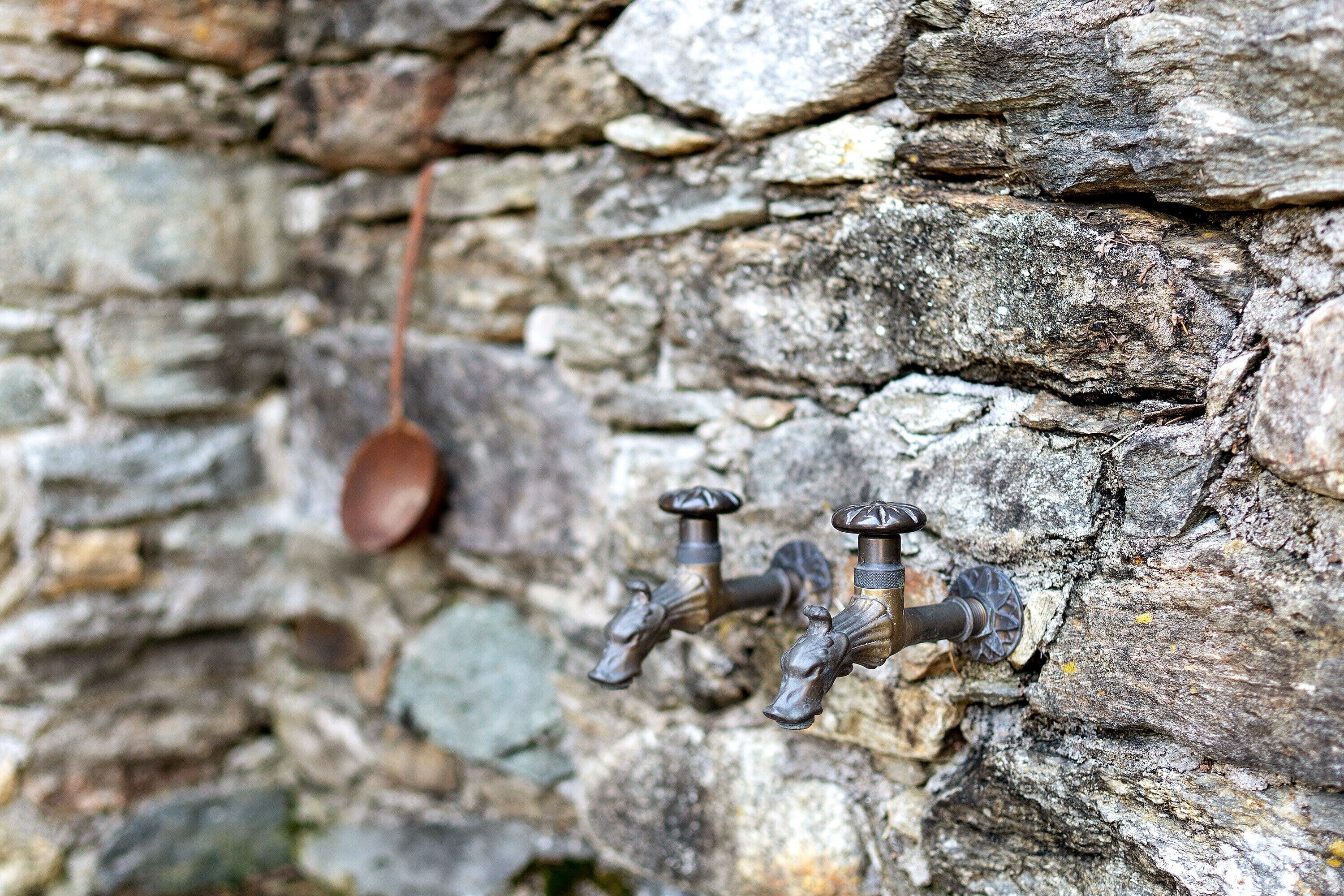 A stone wall with two metal taps and a hanging spoon.
