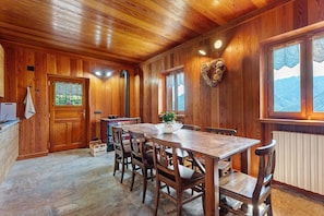 A wooden interior with a dining table and chairs, a window with a view, and a radiator.