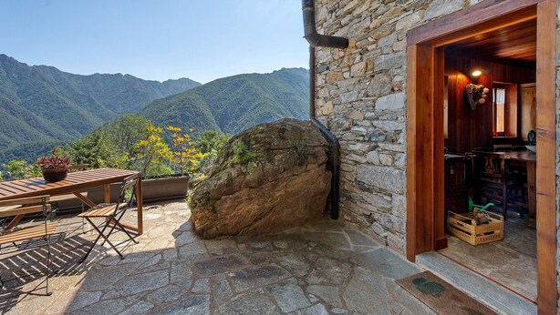 A stone building with a wooden door, a stone table with chairs, and a large rock. - Exclusive Chalet 'La Libellula' with Stunning Mountain Views (Scopello)