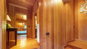 A wooden interior hallway with a bed, a table with a lamp, and a door with a light switch. - Exclusive Chalet 'La Libellula' with Stunning Mountain Views (Scopello)
