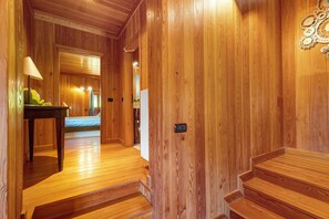 A wooden interior hallway with a bed, a table with a lamp, and a door with a light switch.