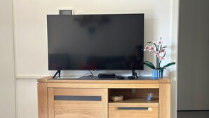 A wooden entertainment center with a flat-screen TV, a remote control, and a decorative orchid plant. - Bright apartment in Verchaix, 4 pers, terrace, garage, Wifi (Verchaix)