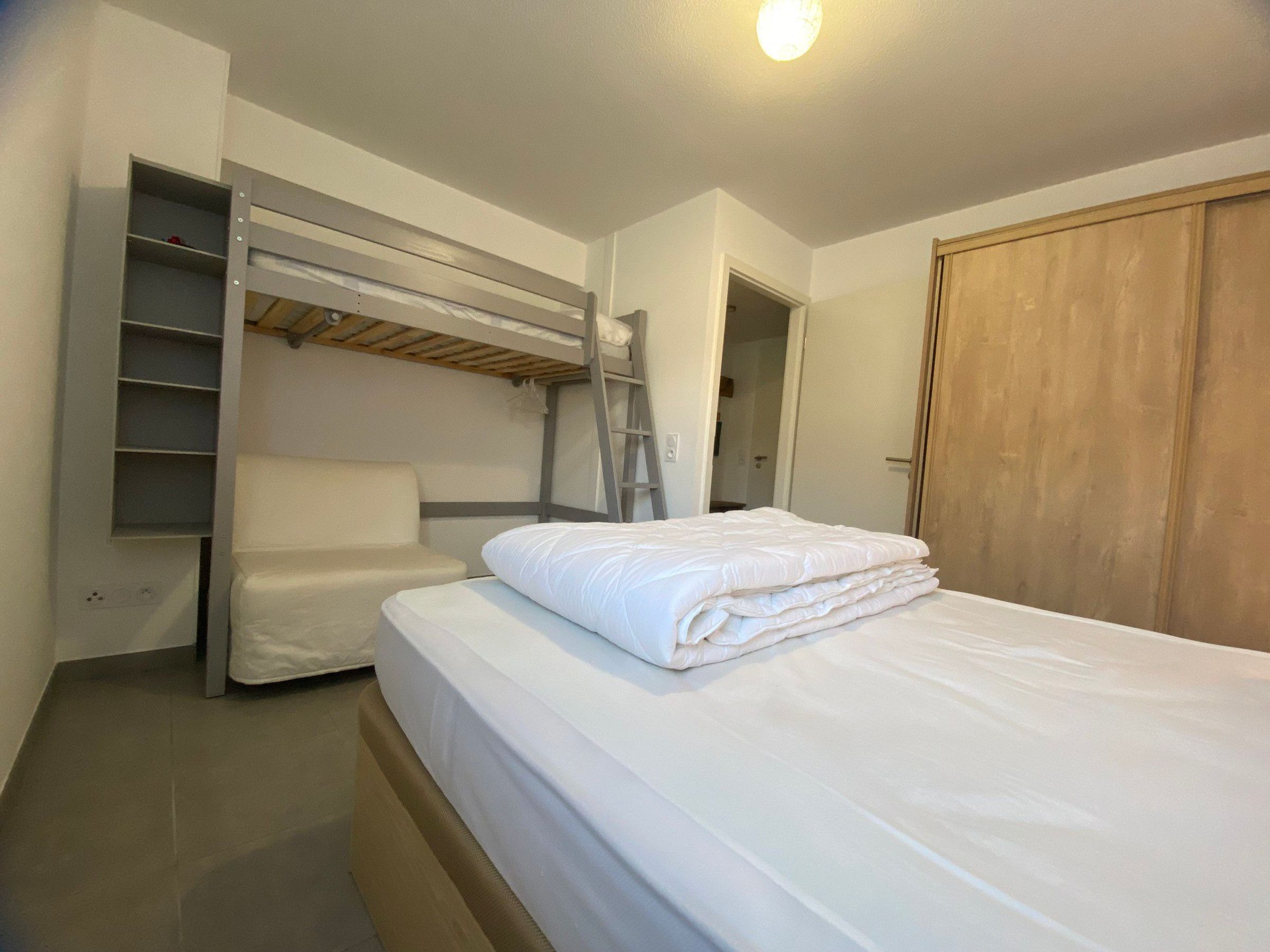 A bedroom with a bunk bed, a chair, a ladder, and a wardrobe.
