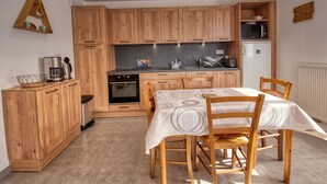 A compact kitchen with wooden cabinets, a dining table with chairs, a coffee maker, and a microwave. - Bright apartment in Verchaix, 4 pers, terrace, garage, Wifi (Verchaix)