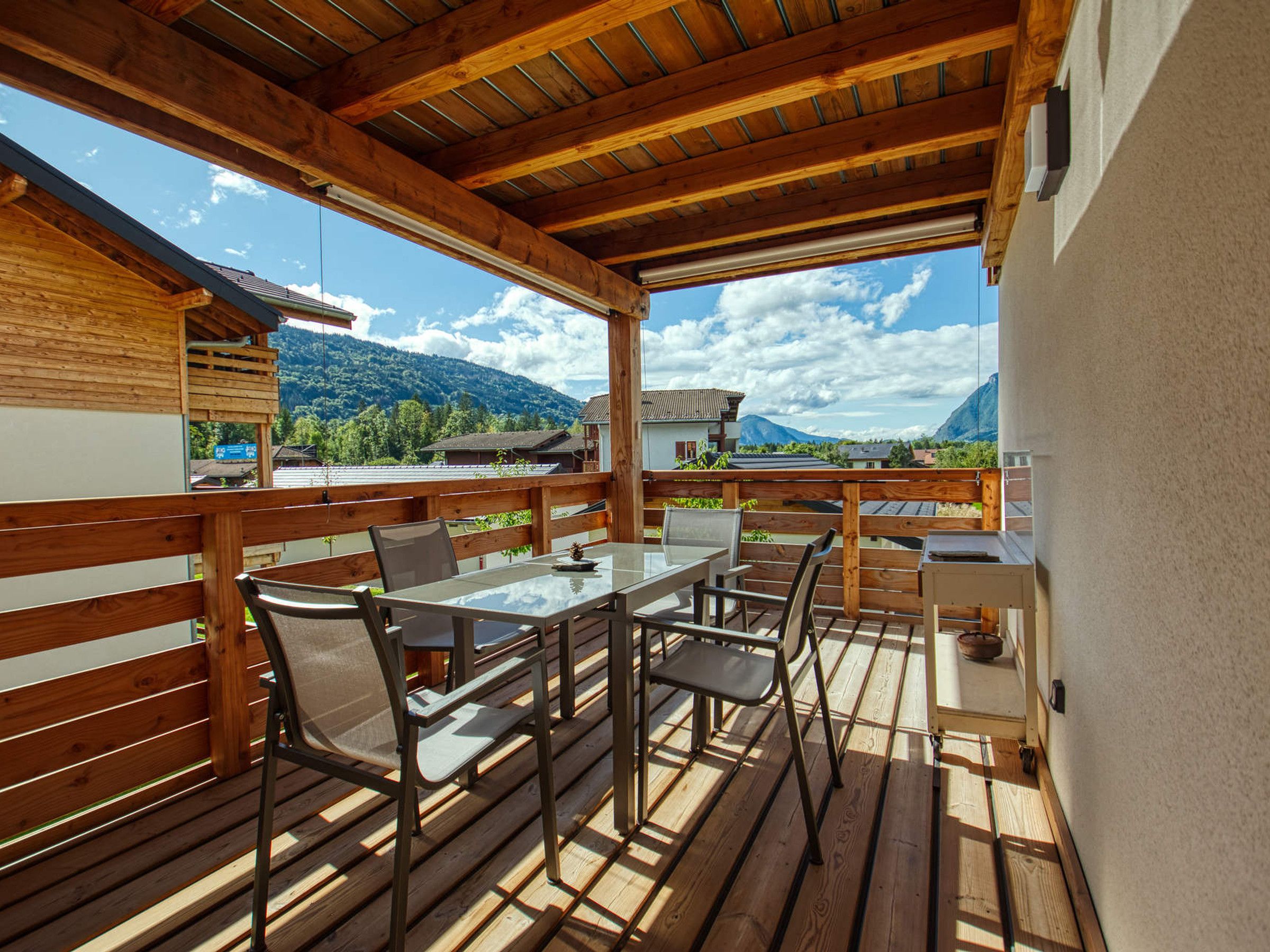 Eine Holzterrasse mit Tisch und Stühlen mit Blick auf eine gebirgige Landschaft.