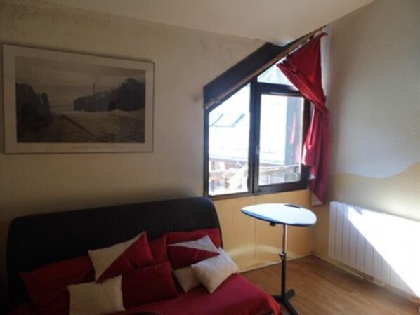 Una habitación con cama, una mesita, una ventana con cortinas y un cuadro en la pared.