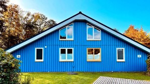 Una casa azul con techo a dos aguas, tres ventanas y el número 56 en el lateral.