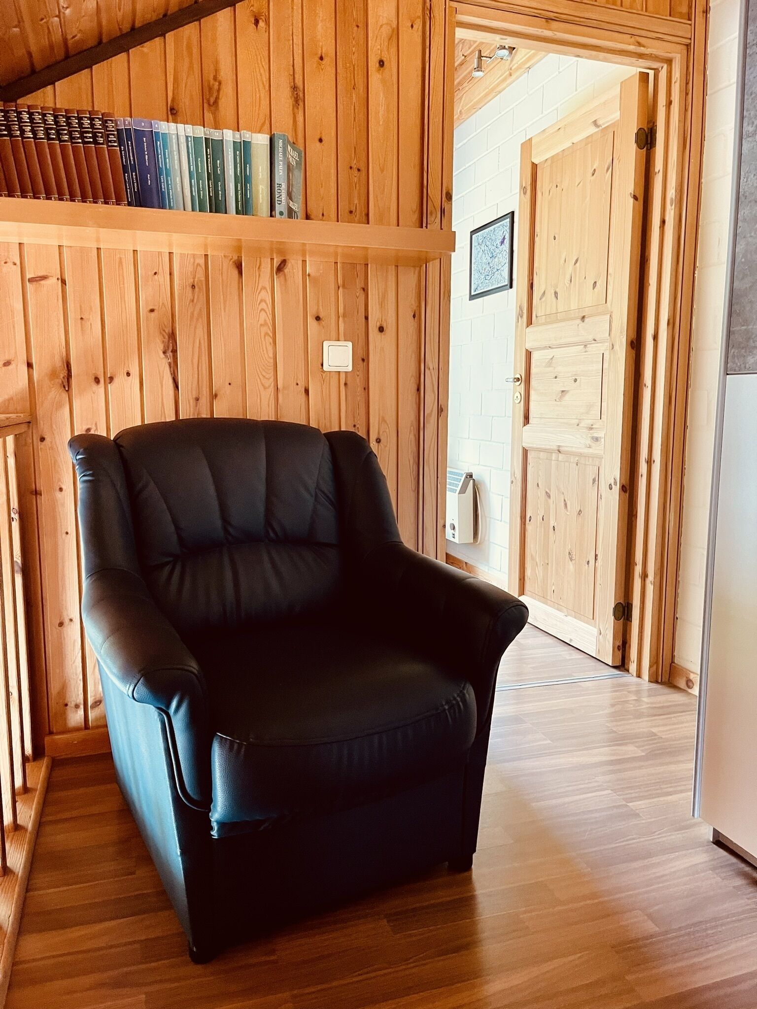 A black leather armchair in a wooden-paneled room with a bookshelf above it.