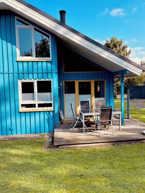 A blue house with a covered patio, a table with chairs, and a chimney. - Premium-ferienhaus im Extertal Ferienpark - Wandern, Natur, Wald, Sauna # (Extertal)