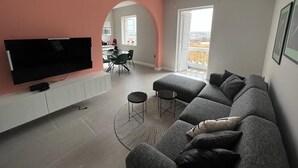 A modern living room with a large flat-screen TV, grey sectional sofa, and a dining area with a table and chairs. - Valletta heart, 3-room superior apartment (Valletta)