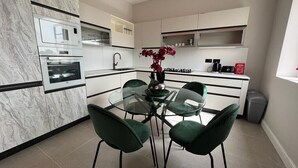 A modern kitchen with a marble backsplash, built-in oven, and a glass dining table with green chairs. - Valletta heart, 3-room superior apartment (Valletta)
