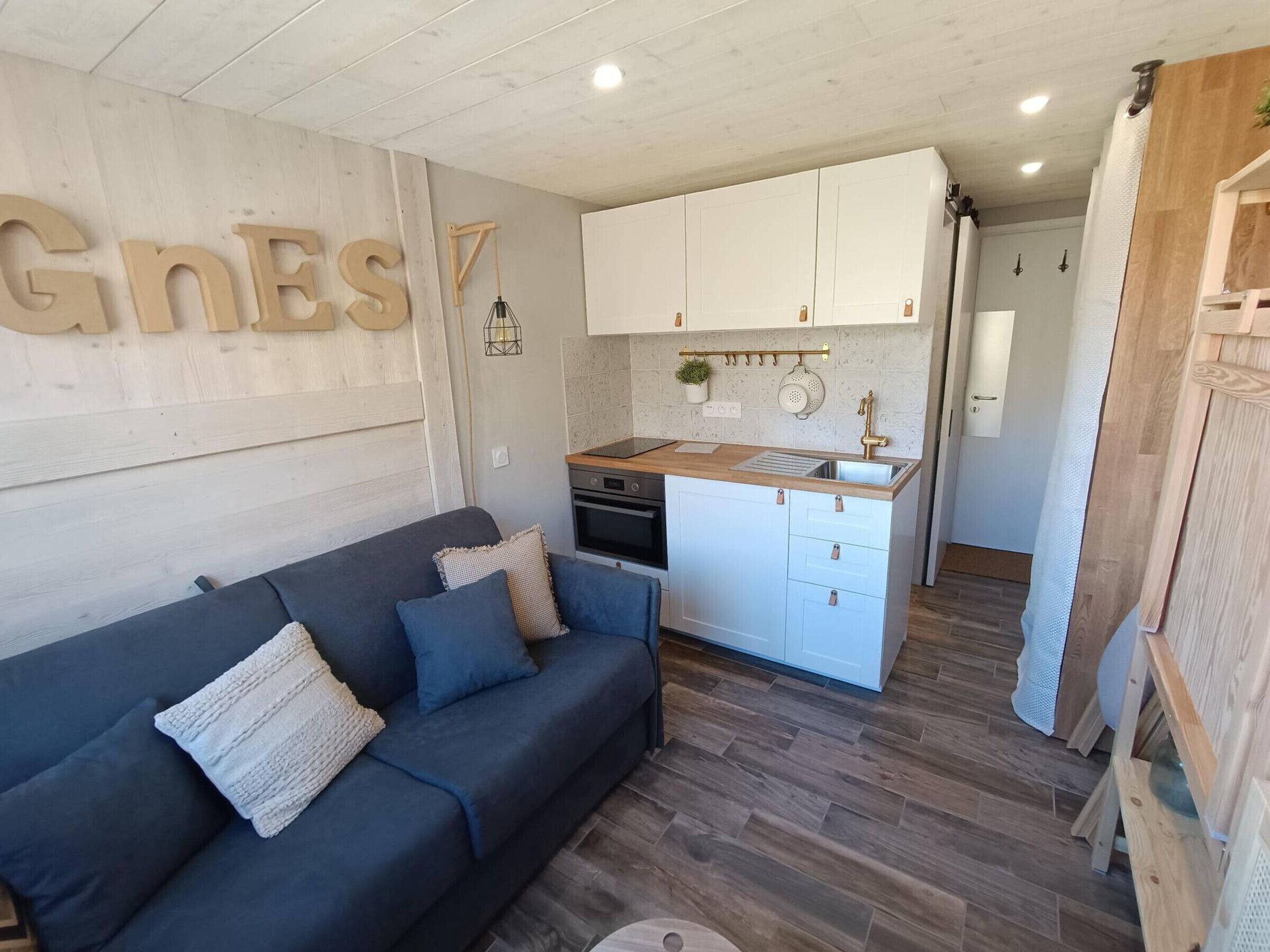 Un espace de vie compact comprenant un coin cuisine, un canapé et un mur en bois orné de lettres.