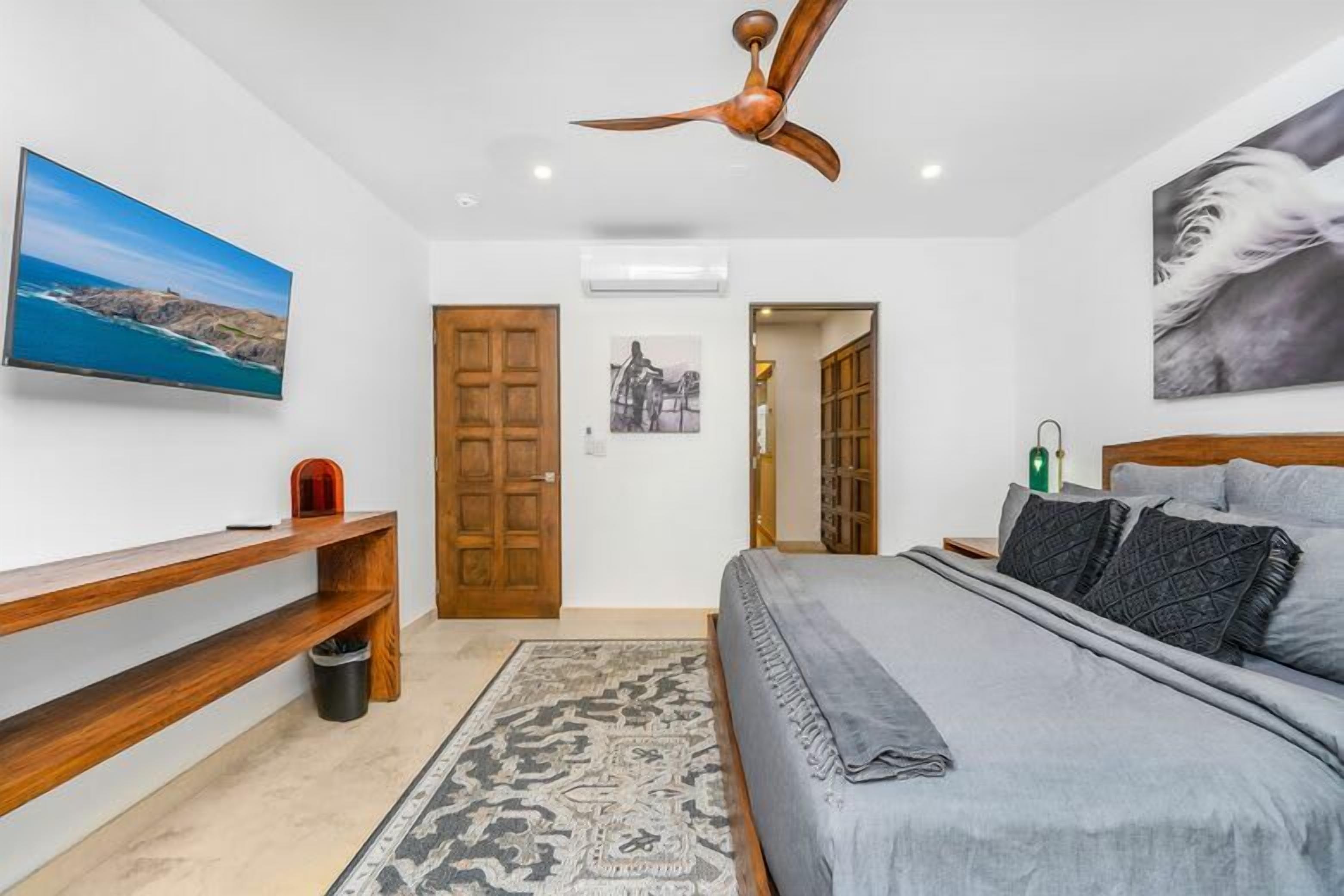 Ein Schlafzimmer mit einem Bett, einer Holzbank, einem Fernseher, einem Deckenventilator und einer Tür zu einem anderen Raum.