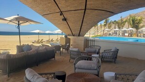 An outdoor lounge area with wicker furniture, umbrellas, and a pool in the background. - Quivira Ocean view private villa with pool (Cabo San Lucas)