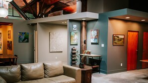 A spacious living area with a leather sofa, a wooden coffee table, and a bookshelf. There are framed artworks on the walls and a door with a red frame.