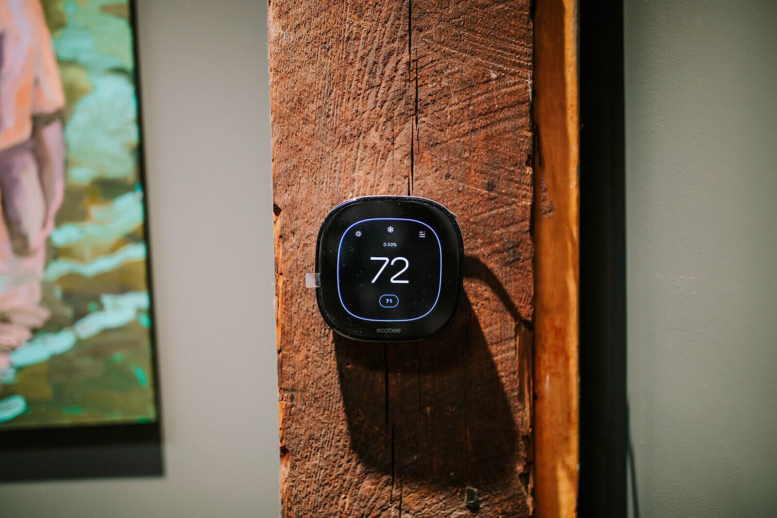 Een thermostaat bevestigd aan een houten oppervlak, waarop een temperatuur van 72 graden wordt weergegeven.