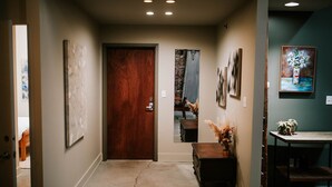A hallway with a wooden door, a small table with a vase, and a painting on the wall.