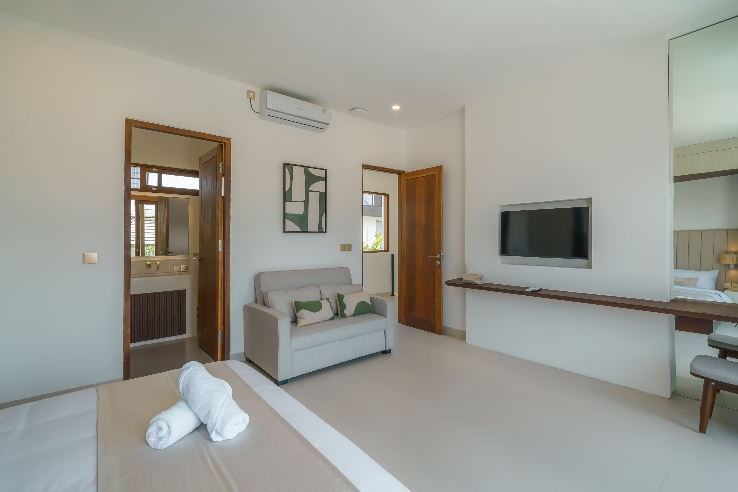 A modern hotel room with a bed, a sofa, a TV, and a desk.