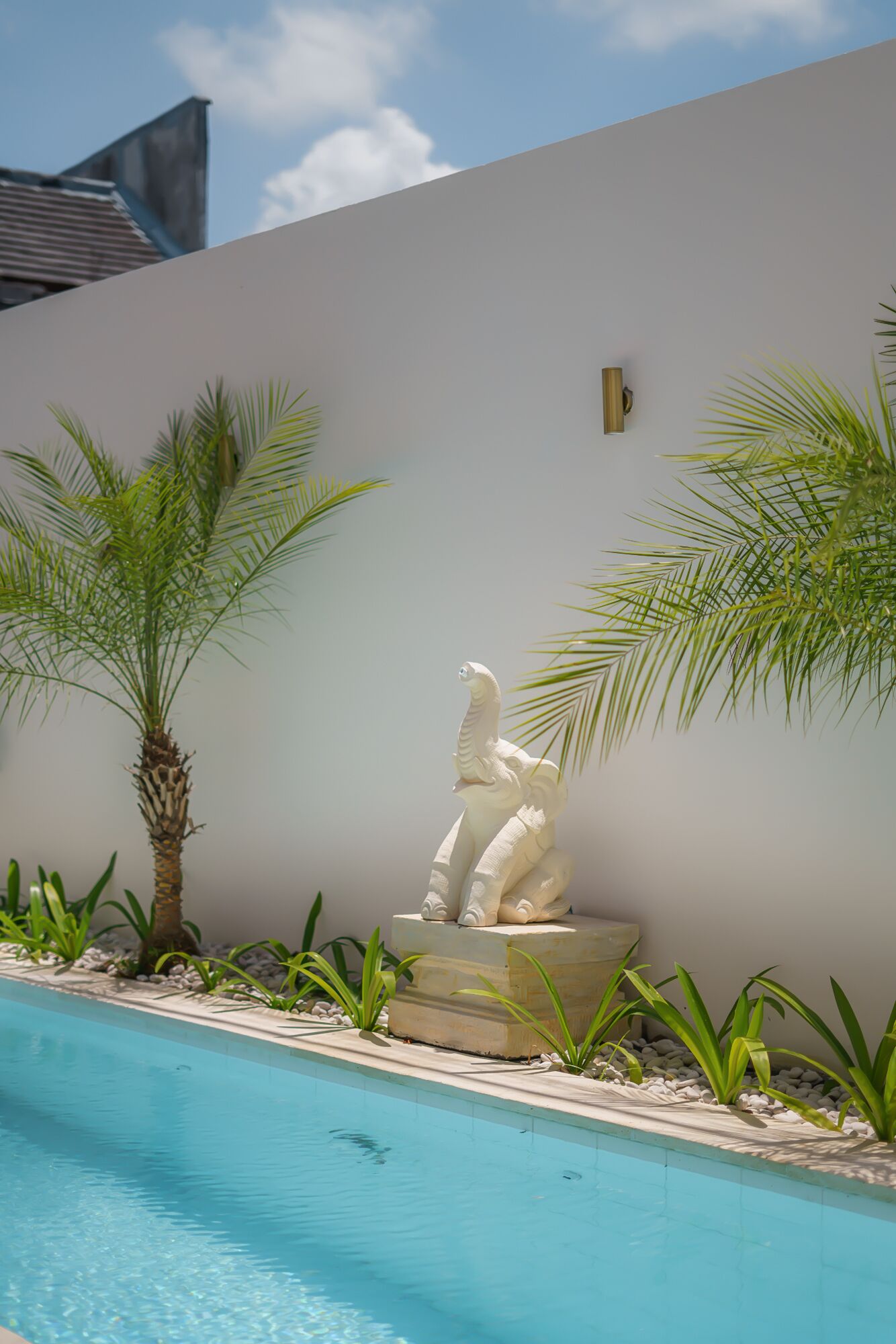 A pool with a white sculpture of a figure on a pedestal, surrounded by palm trees and plants.