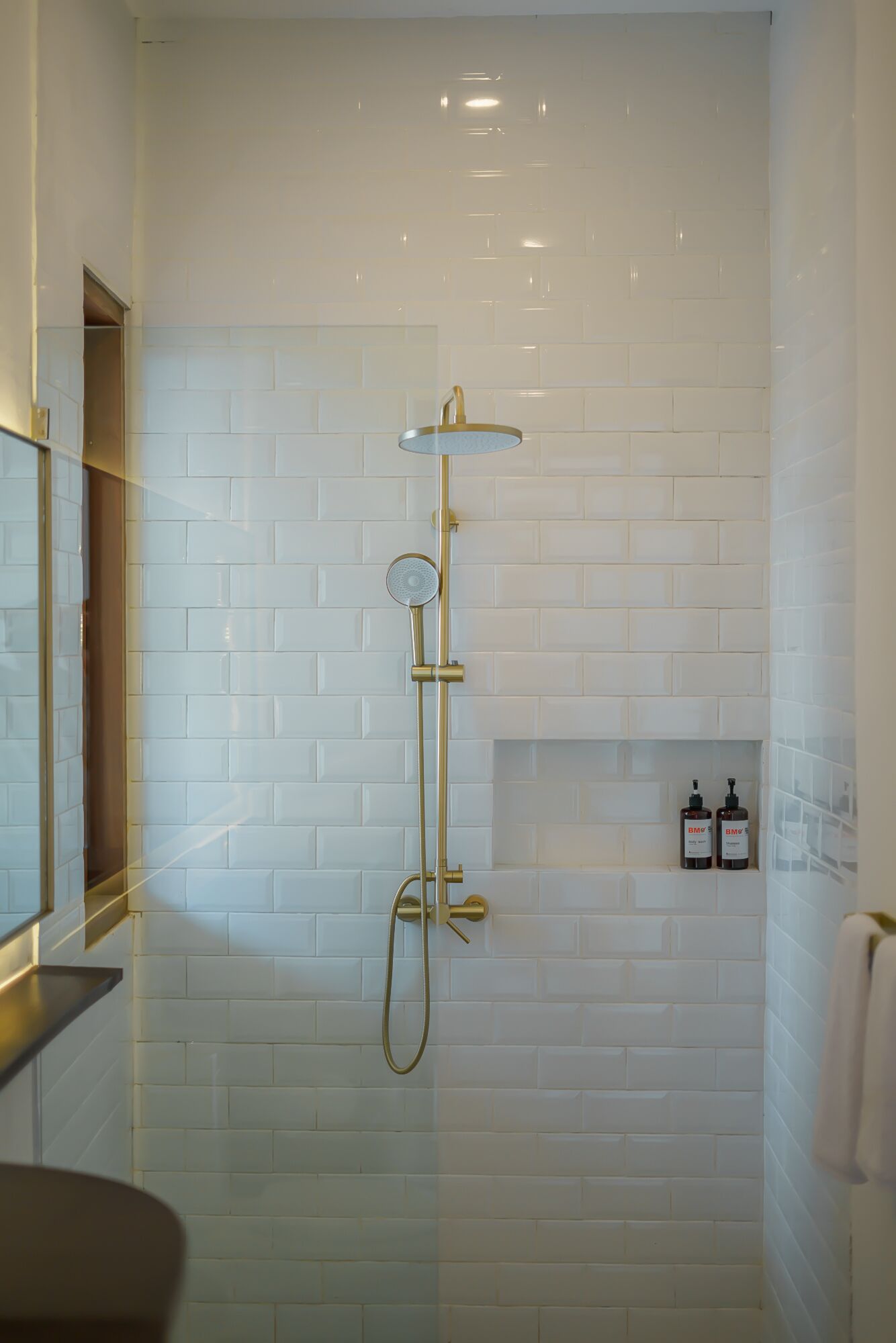 A modern bathroom with white subway tiles, a gold showerhead, and a handheld shower.