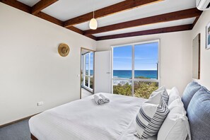 A bedroom with a large bed, a view of the ocean, and a wooden ceiling structure.