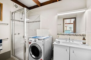 A compact bathroom with a glass shower enclosure, a built-in washing machine, and a sink with a mirror above it.