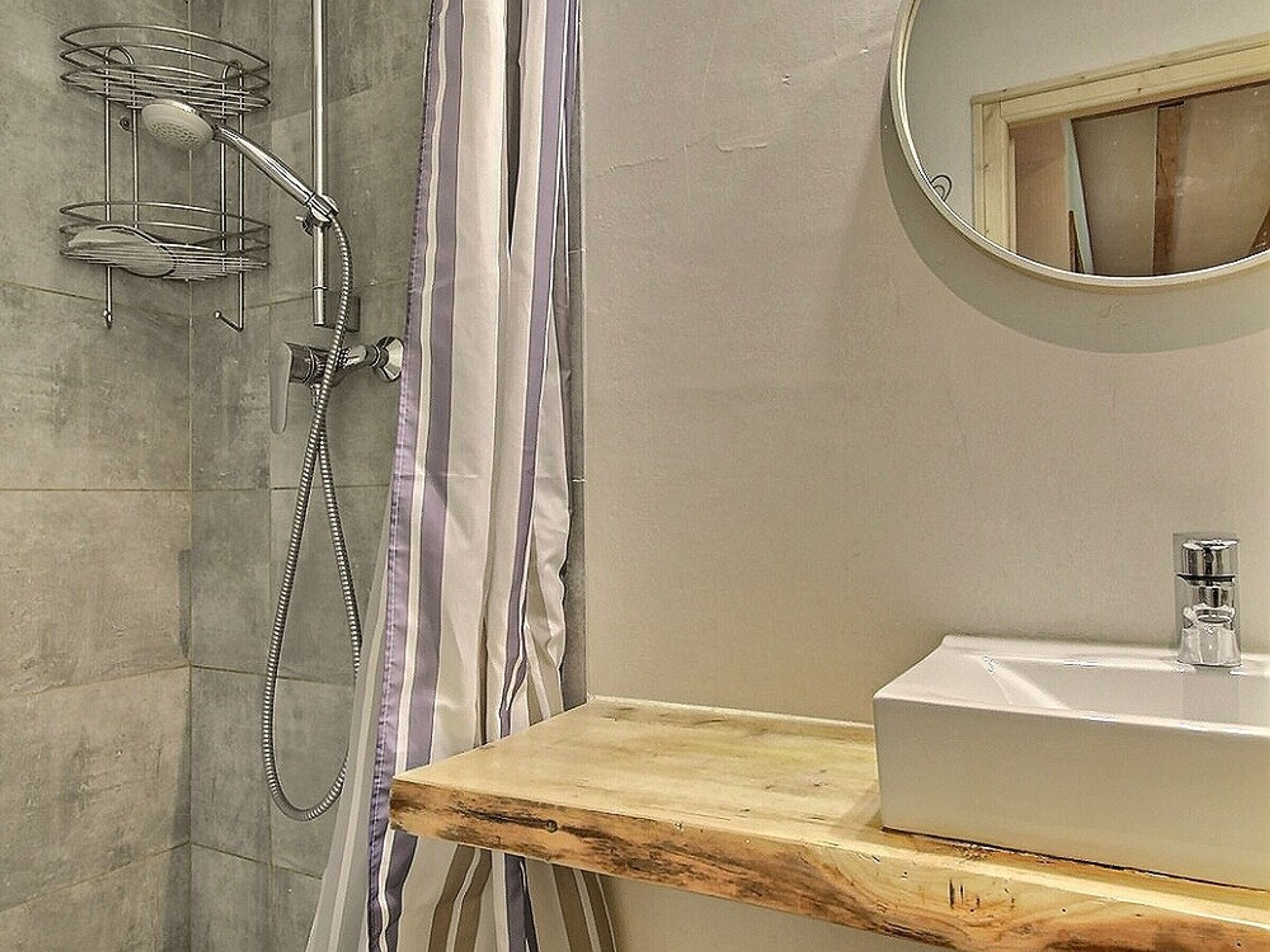 Une salle de bain avec une douche, un meuble-lavabo en bois et un miroir rond.