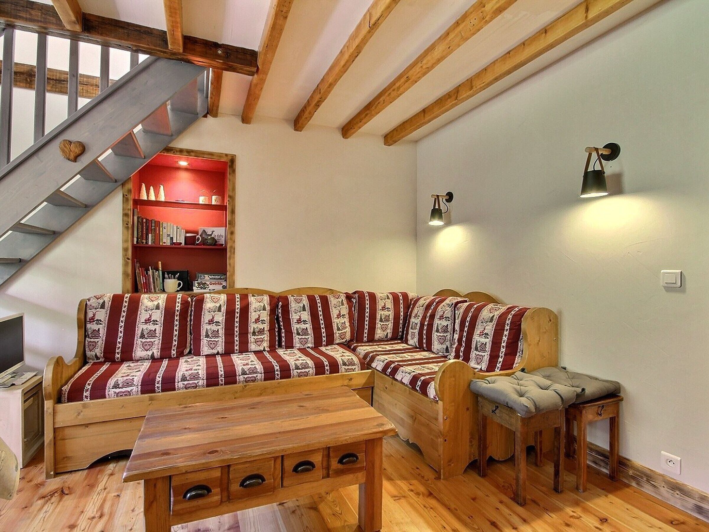 Ein gemütliches Wohnzimmer mit einem Holzsofa, einem kleinen Tisch und einer Treppe, die zu einem roten Bücherregal führt.