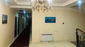 Un couloir orné d’un lustre, d’un radiateur et d’un tableau représentant une vue panoramique d’une ville.