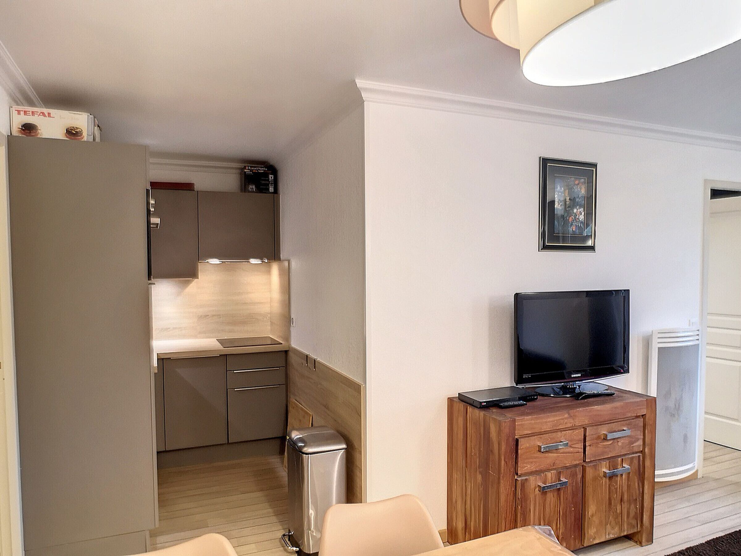 Pieni hotellihuone, jossa on minikeittiö, televisio puukehikossa ja seinällä oleva taulu.