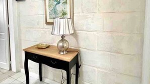 A hallway with a tiled floor, a small table with a lamp, a framed picture on the wall, and a sign that reads "Bermuda". - Cottonera cara guesthouse (Bormla)
