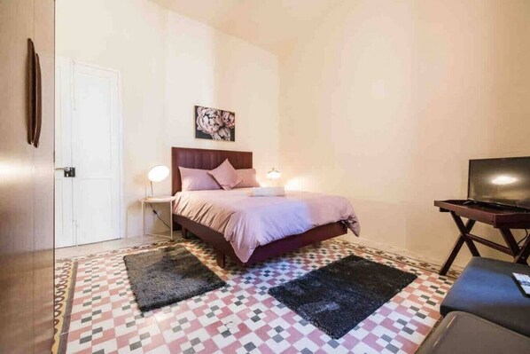 Un dormitorio con cama, lámparas de noche, televisor y una alfombra estampada.