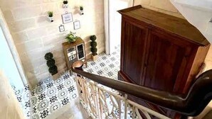 A staircase with a white railing, a wooden cabinet, and a wall with a brick pattern. - Cottonera cara guesthouse (Bormla)