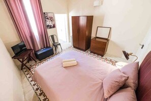 Un dormitorio con cama, escritorio, silla, armario y lámpara.